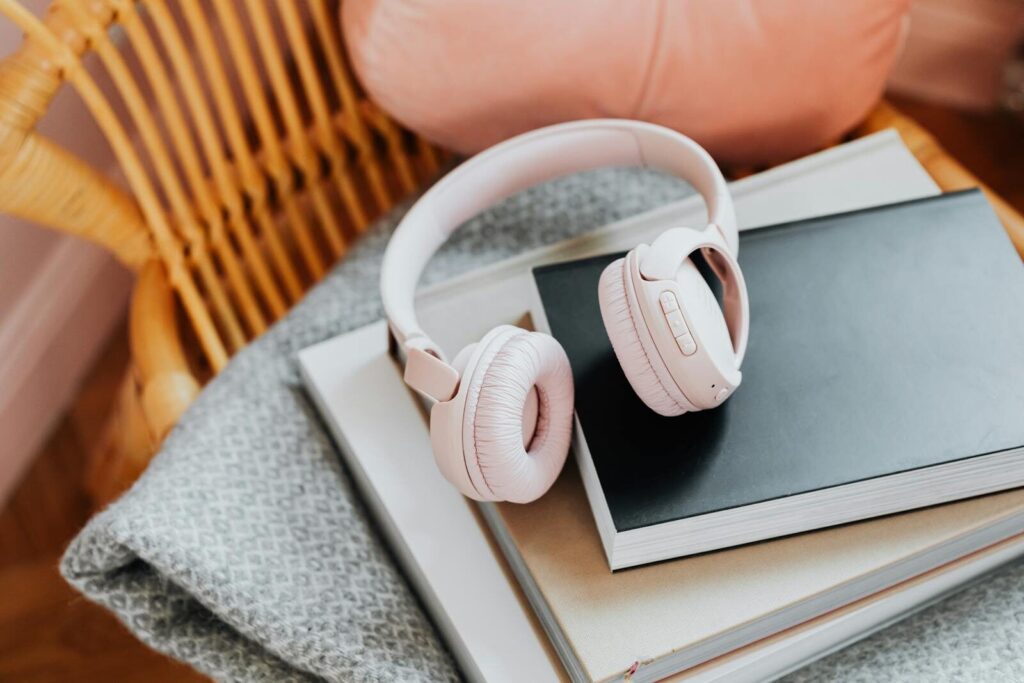 Pink wireless headphones resting on a stack of books on a rattan chair, enhancing a cozy vibe.
